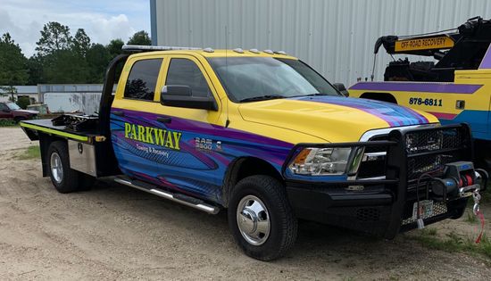 Yellow and blue Parkway Towing truck parked in front of a building.