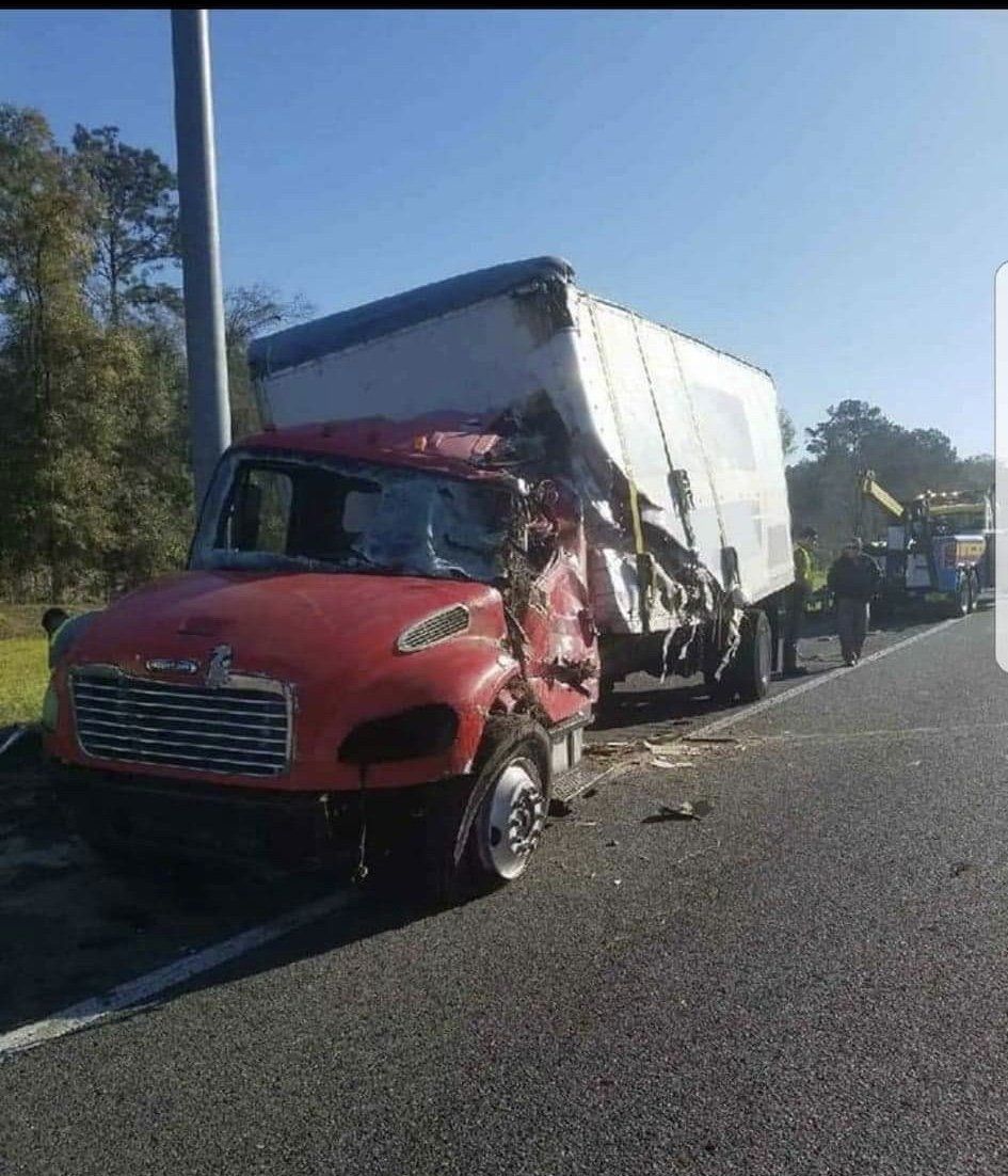 Red semi-truck damaged on highway after collision; white trailer crushed on the side.