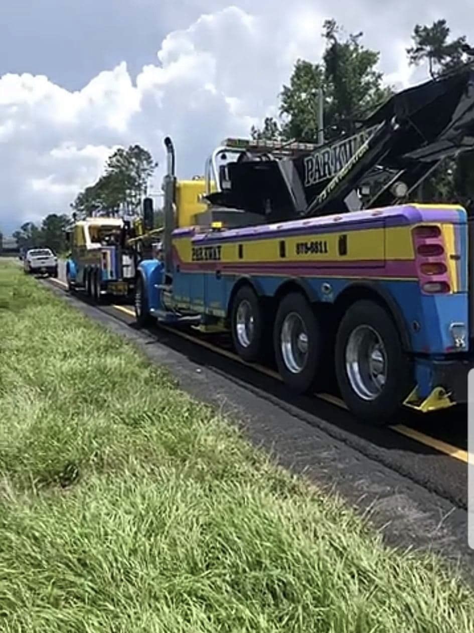 A large tow truck with yellow, purple, and blue paint is towing a small vehicle on a roadside.