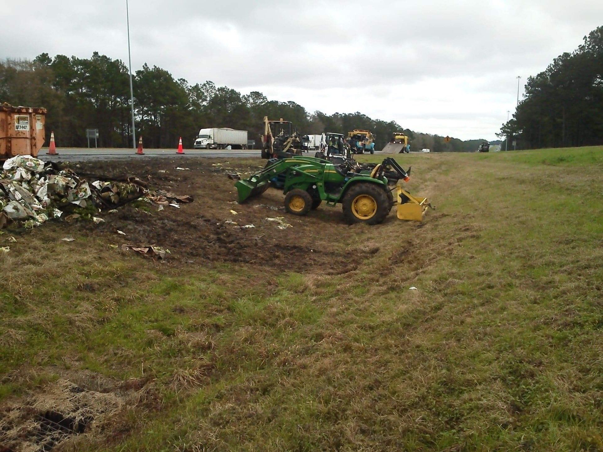 A John Deere tractor working on the side of a highway on a cloudy day.