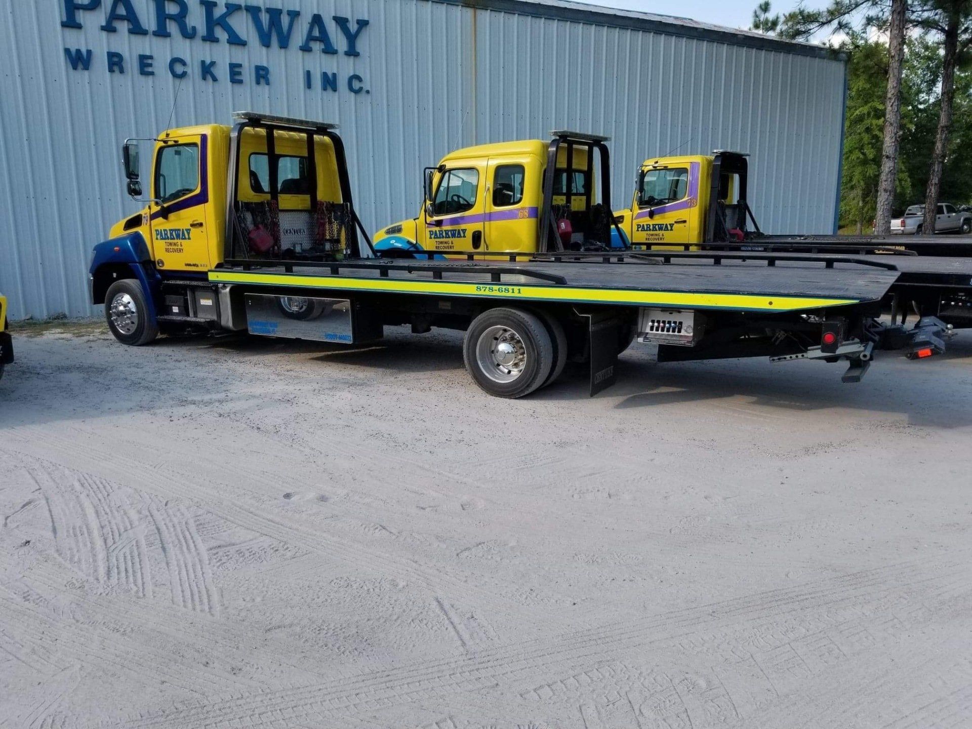 Three yellow tow trucks parked outside a building with 
