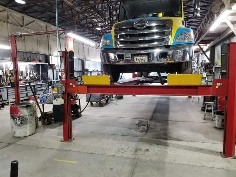 A truck elevated on a red car lift inside a brightly lit repair shop.