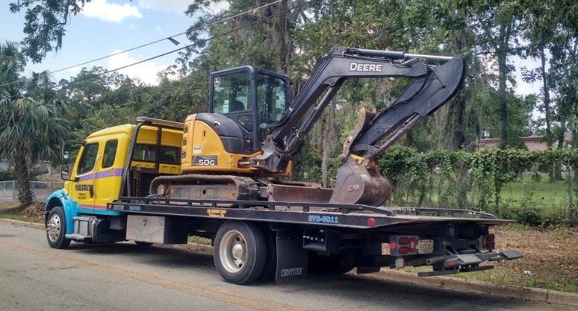 Yellow tow truck transporting a yellow and black excavator on a flatbed trailer.