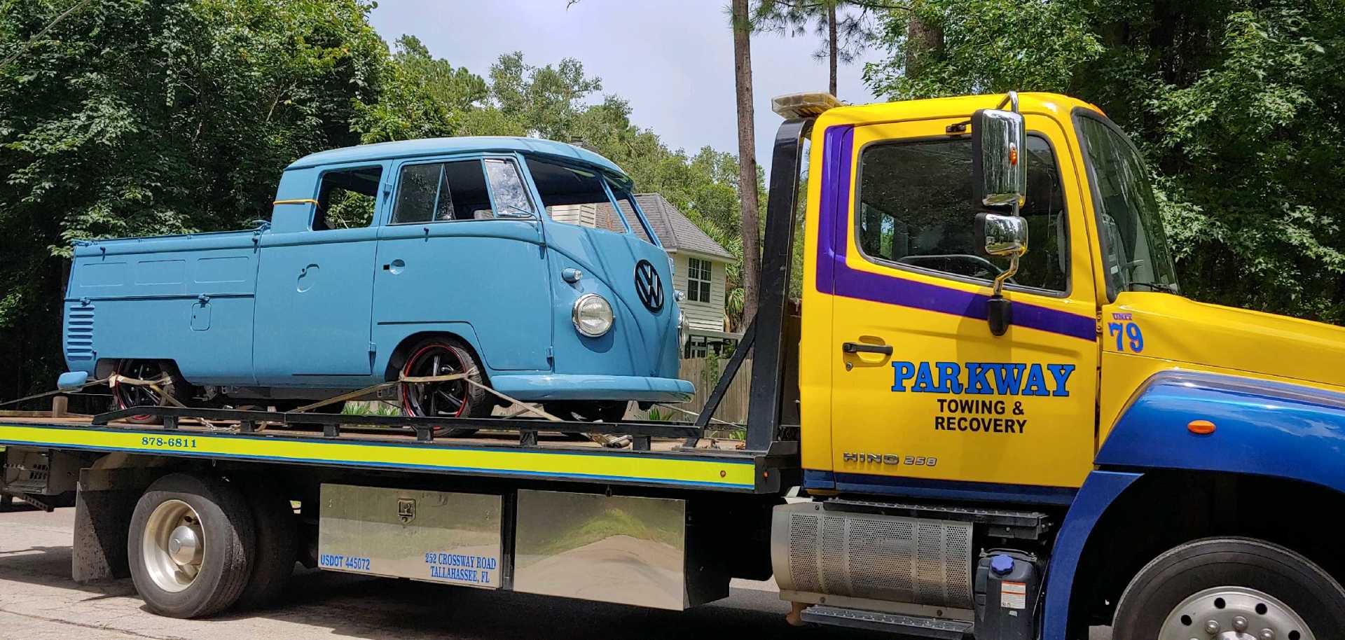 A light blue VW pickup truck is loaded onto a yellow tow truck. The tow truck has 