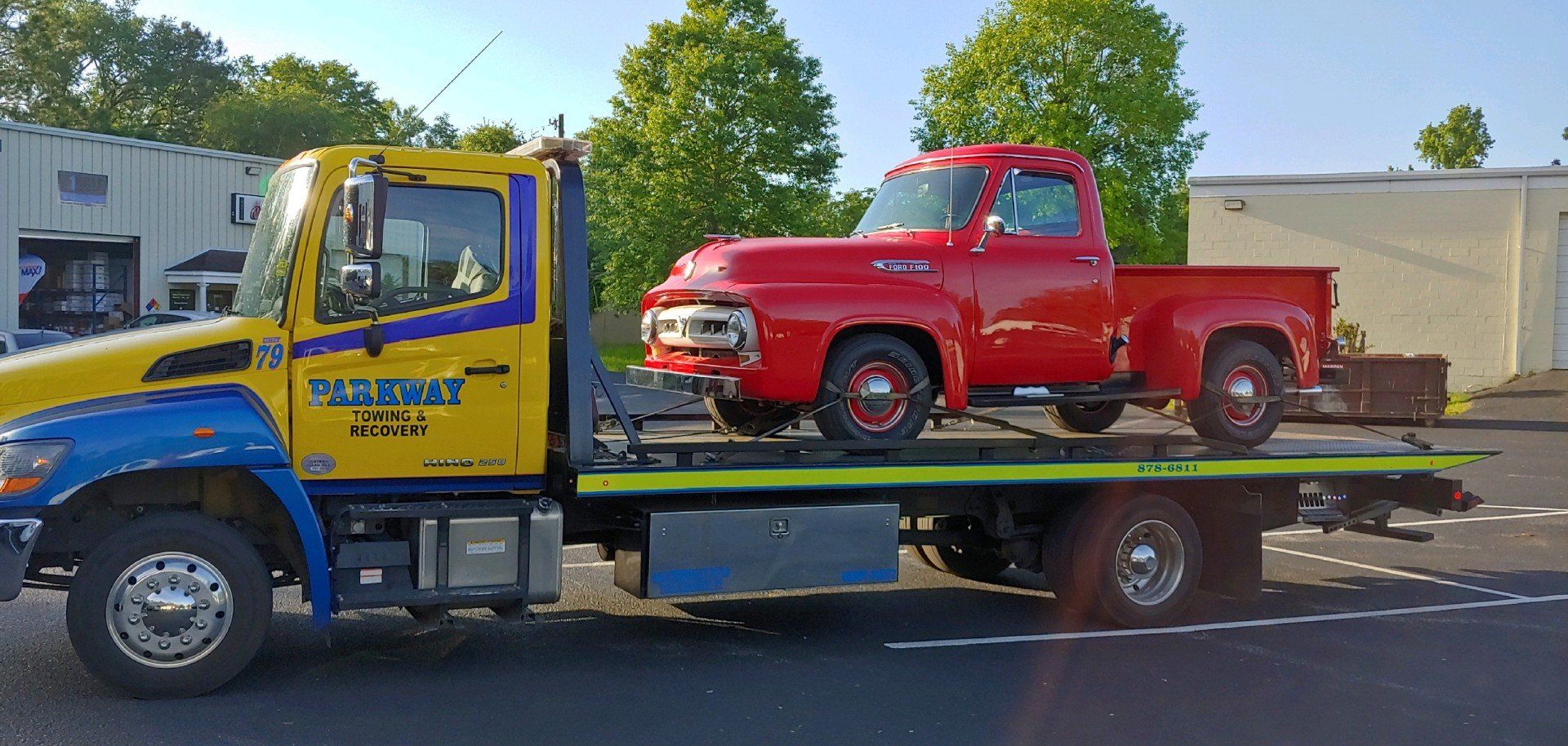 Red classic pickup truck being transported on a yellow and blue tow truck.