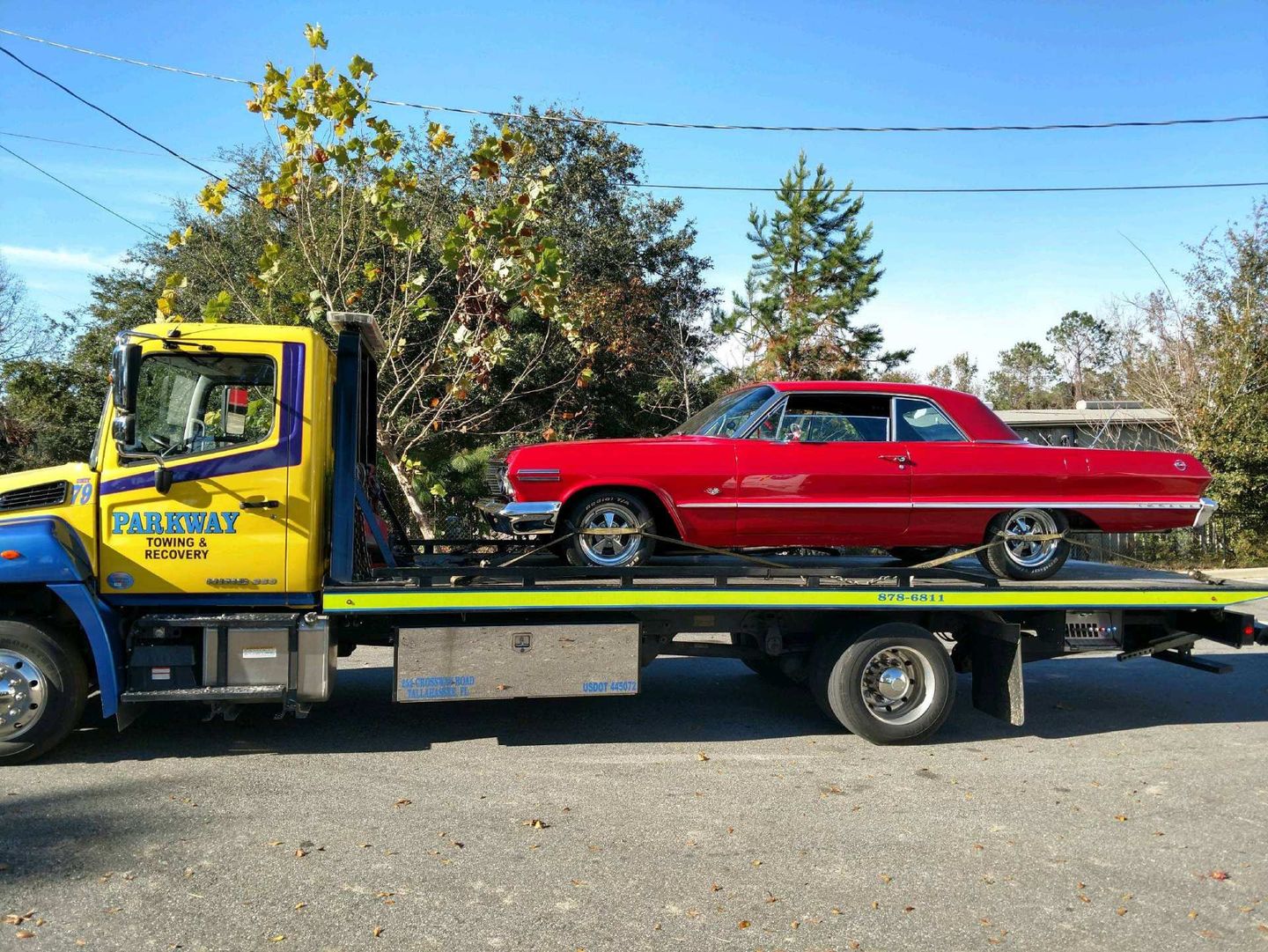 Red classic car on a flatbed tow truck. Yellow and blue truck, sunny day.