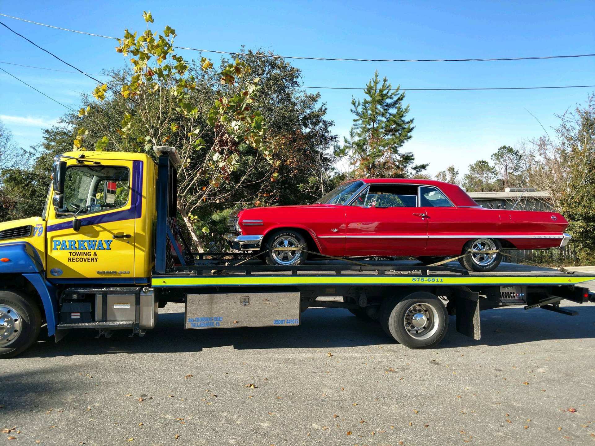 Red classic car on a flatbed tow truck. Yellow and blue truck, sunny day.
