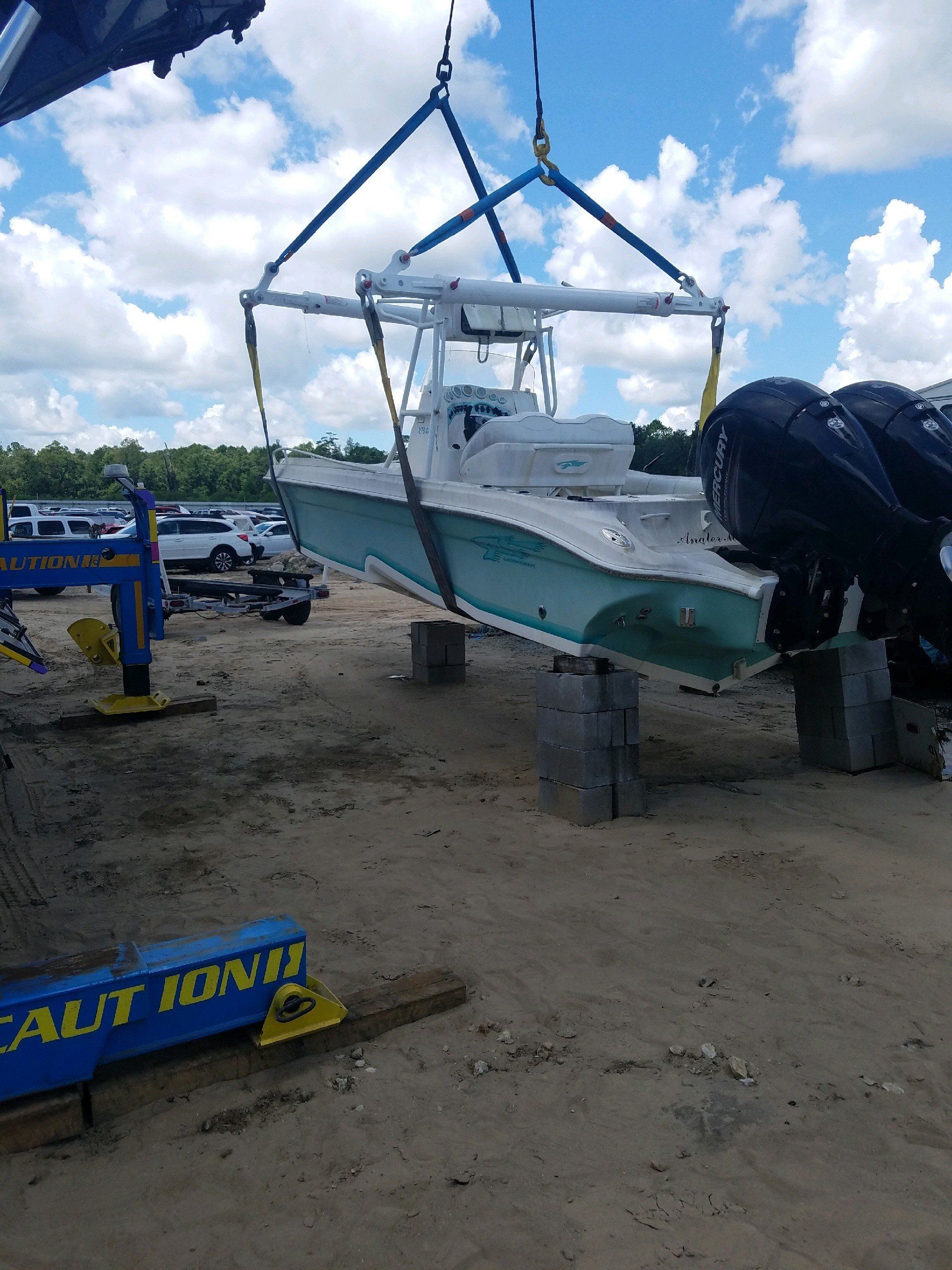 A boat suspended by a crane. Blue and white boat lifted over cinder blocks. Sunny day.
