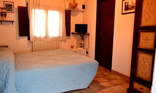Una stanza con un letto matrimoniale, un tv sulla mensola, una finestra aperta e aria condizionata al muro