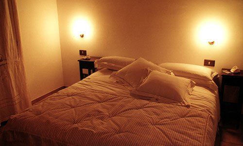 Un letto matrimoniale con piumone,cuscini bianchi e due luci accese sopra comodini