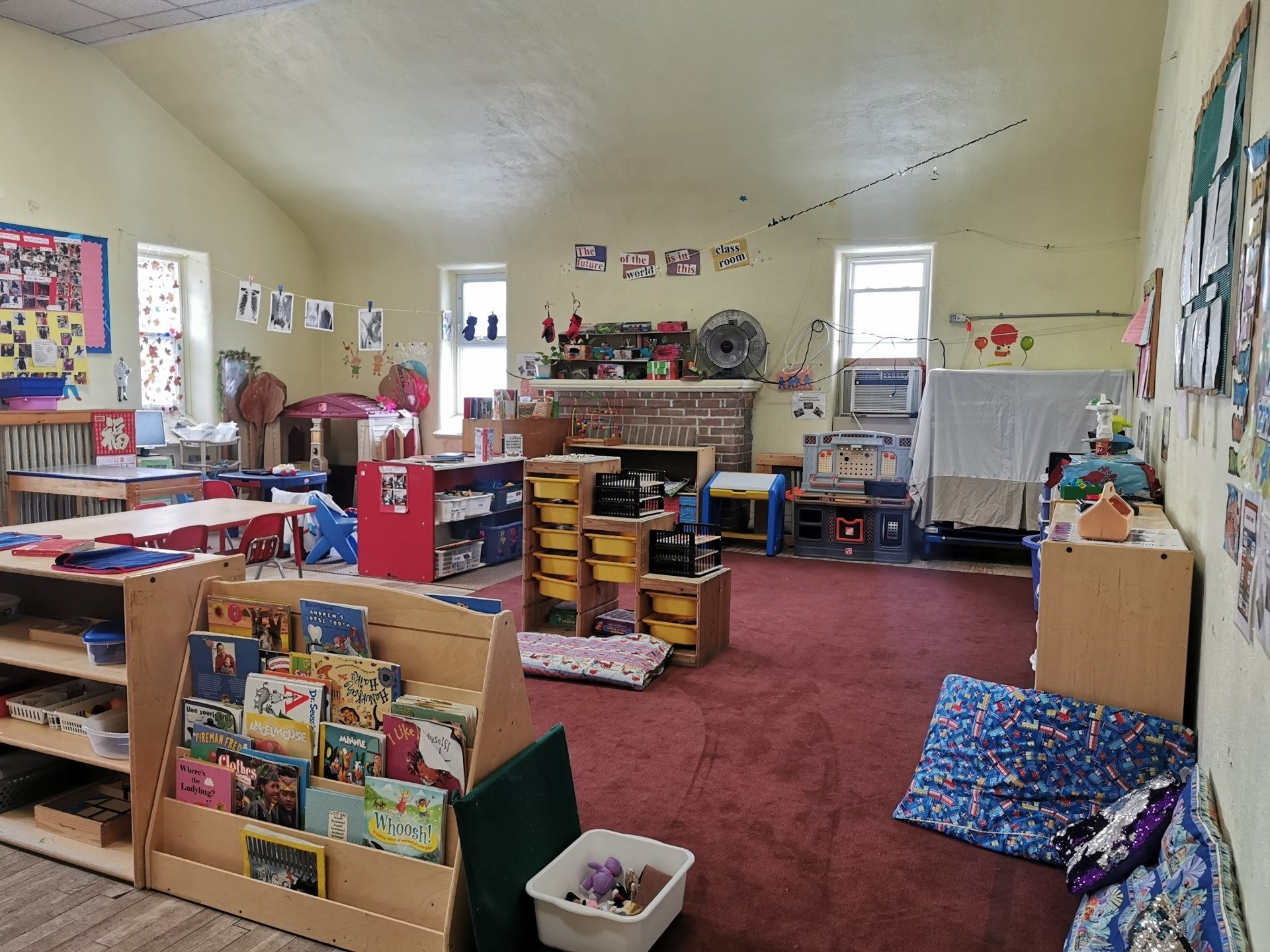 Red carpeted daycare room with book shelf and round tables