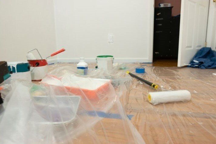 Picture of a painting contractors rolling pin and paint tray sitting on a hard wood floor with drop cloths