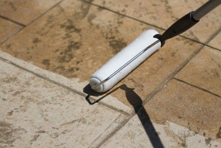 Exterior stone tile patio being sealed with a pole roller