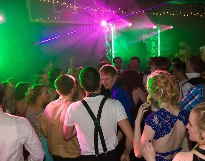 A crowd of people are dancing in a dark room with green and purple lights