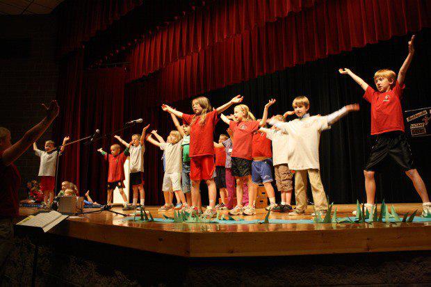 A group of children are standing on a stage with their arms in the air