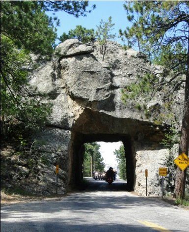 A person riding a motorcycle under a rock tunnel