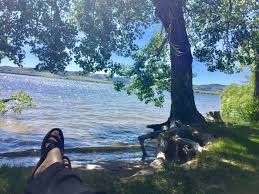 A person is laying on the grass near a lake with their feet up.