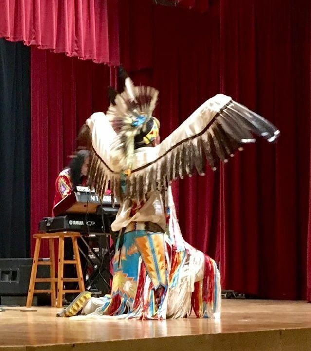 A person is kneeling on a stage with their wings outstretched