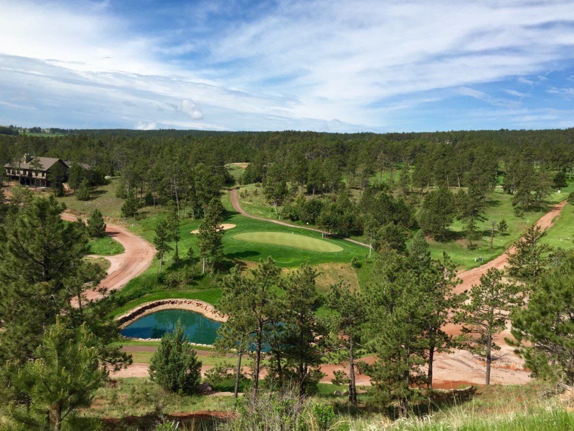 An aerial view of a golf course surrounded by trees and a pond.