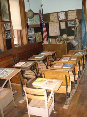 A classroom with wooden desks and chairs with books on them