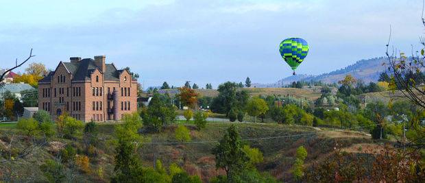 A hot air balloon is flying over a large building in the distance.