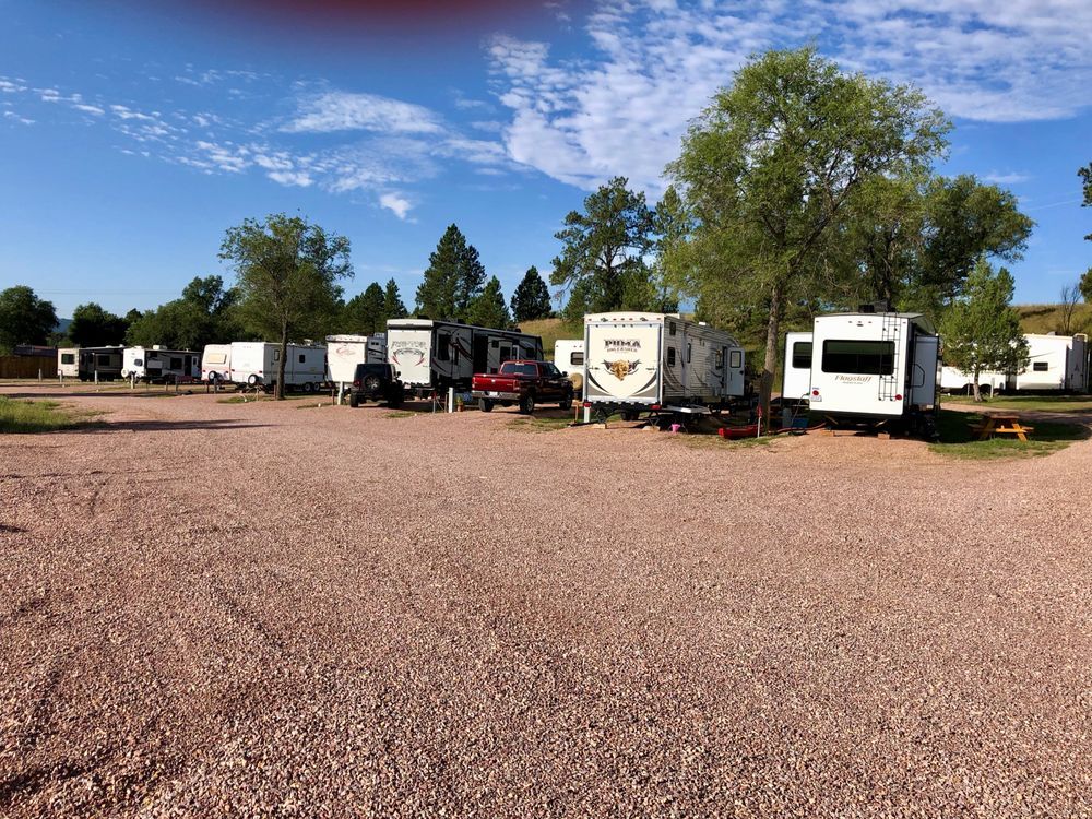 A row of rvs are parked in a gravel lot.
