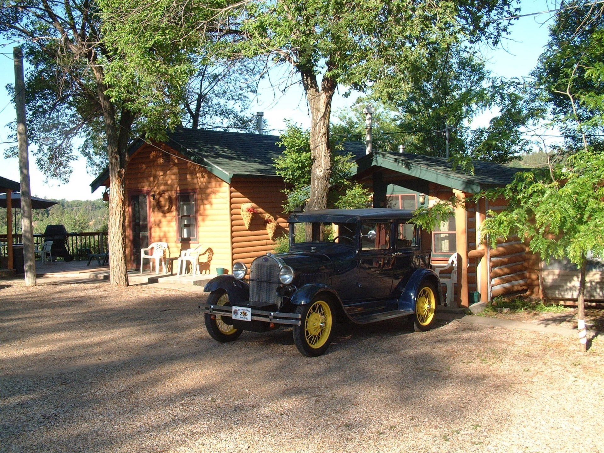 An old car is parked in front of a log cabin