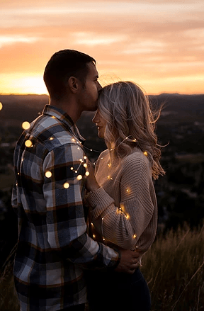 A man is kissing a woman on the forehead while holding a string of lights.