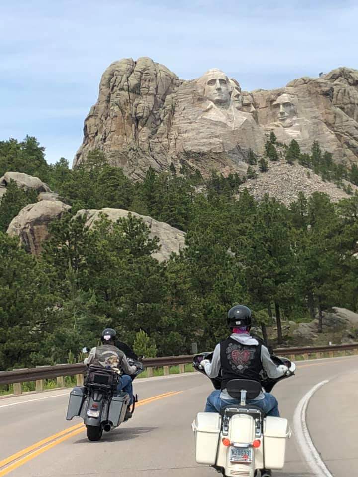 Two people are riding motorcycles down a road in front of a mountain.