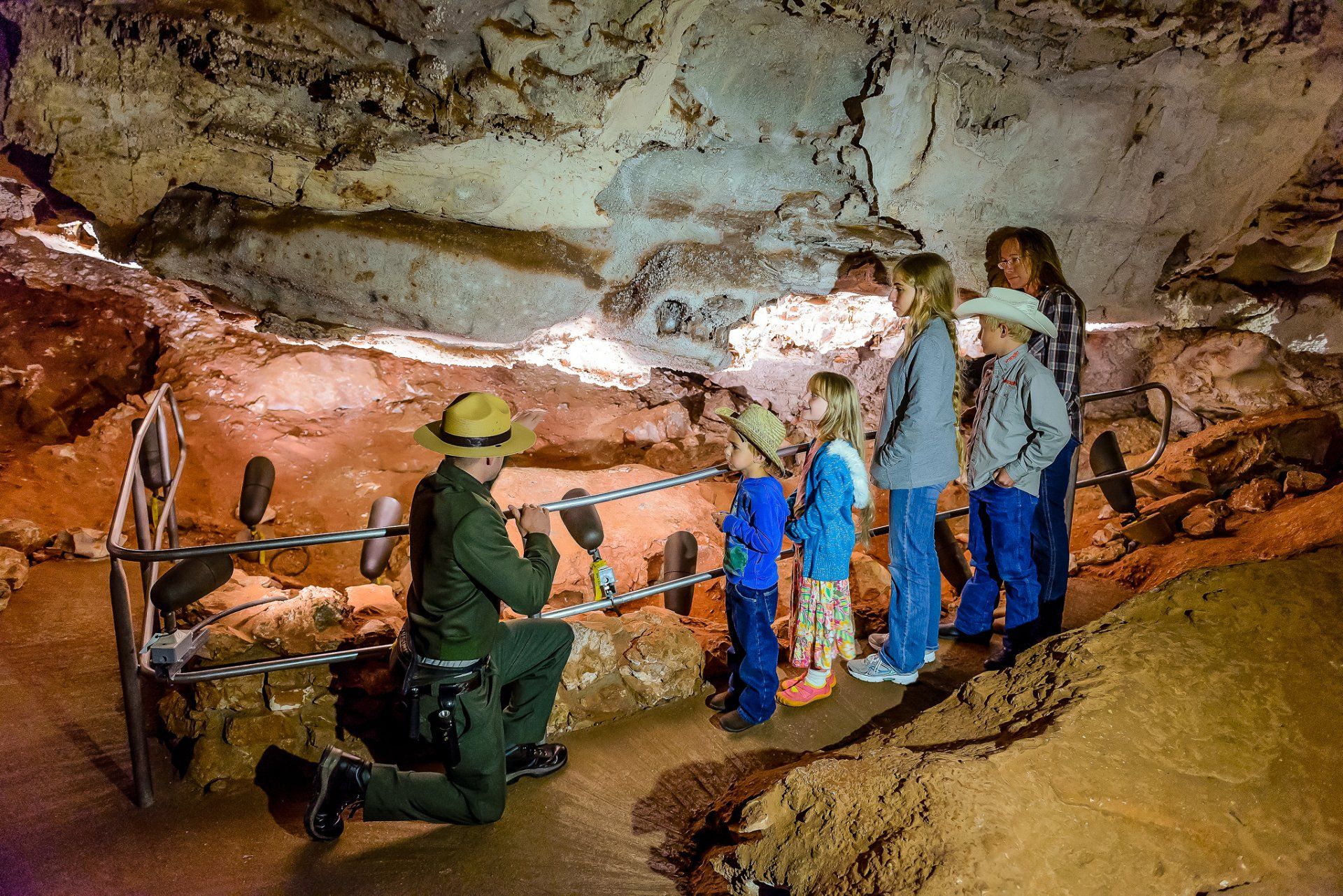 A man is kneeling down in front of a group of people in a cave.