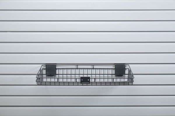 A wire basket is hanging on a slat wall.