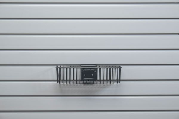 A black basket is hanging on a white wall.