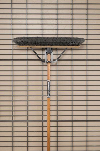 A broom with a wooden handle is against a brick wall.