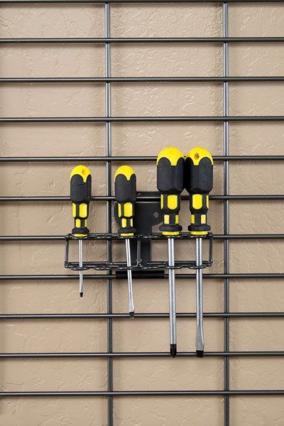 Four screwdrivers are hanging on a wire rack on a wall.