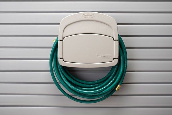 A green hose is hanging from a hook on a wall.