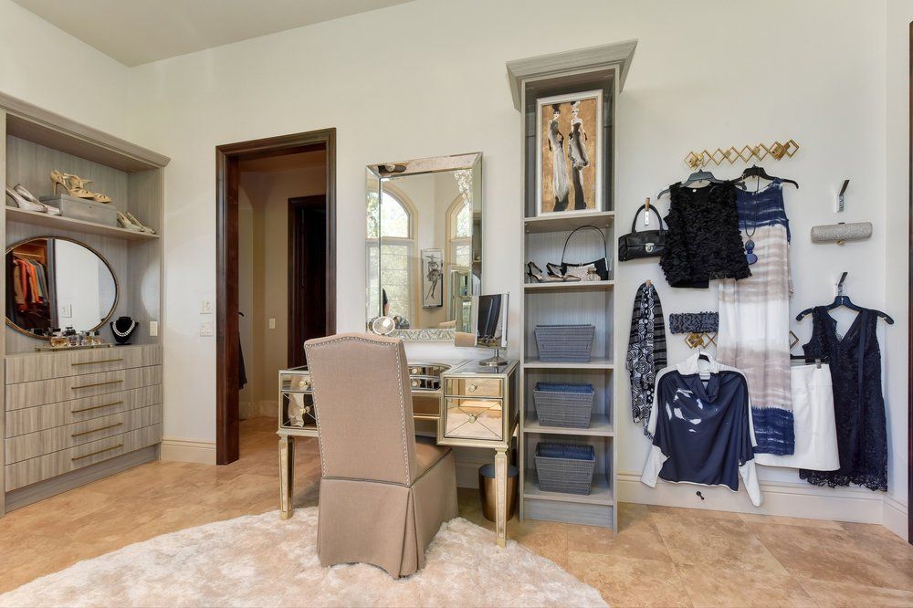 A walk in closet with a vanity , chair , mirror and clothes hanging on the wall.