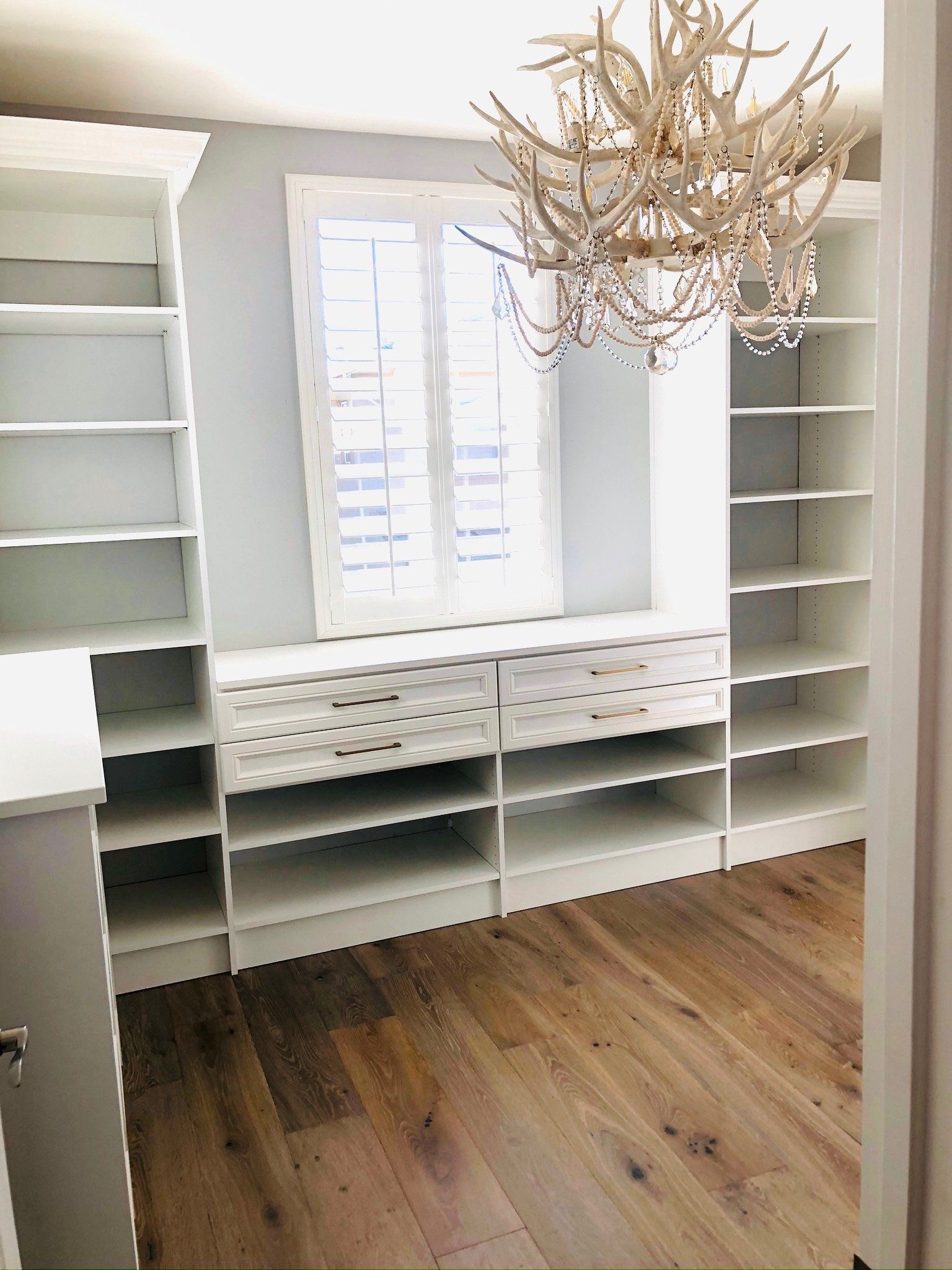 A walk in closet with lots of shelves and drawers and a chandelier hanging from the ceiling.