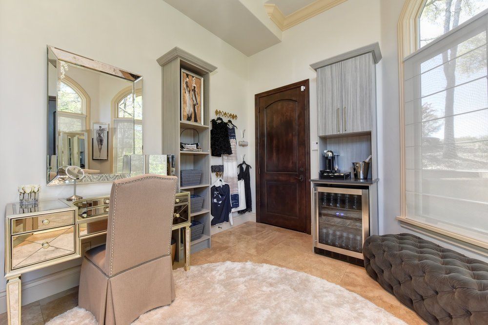 A dressing room with a vanity , chair , mirror and ottoman.