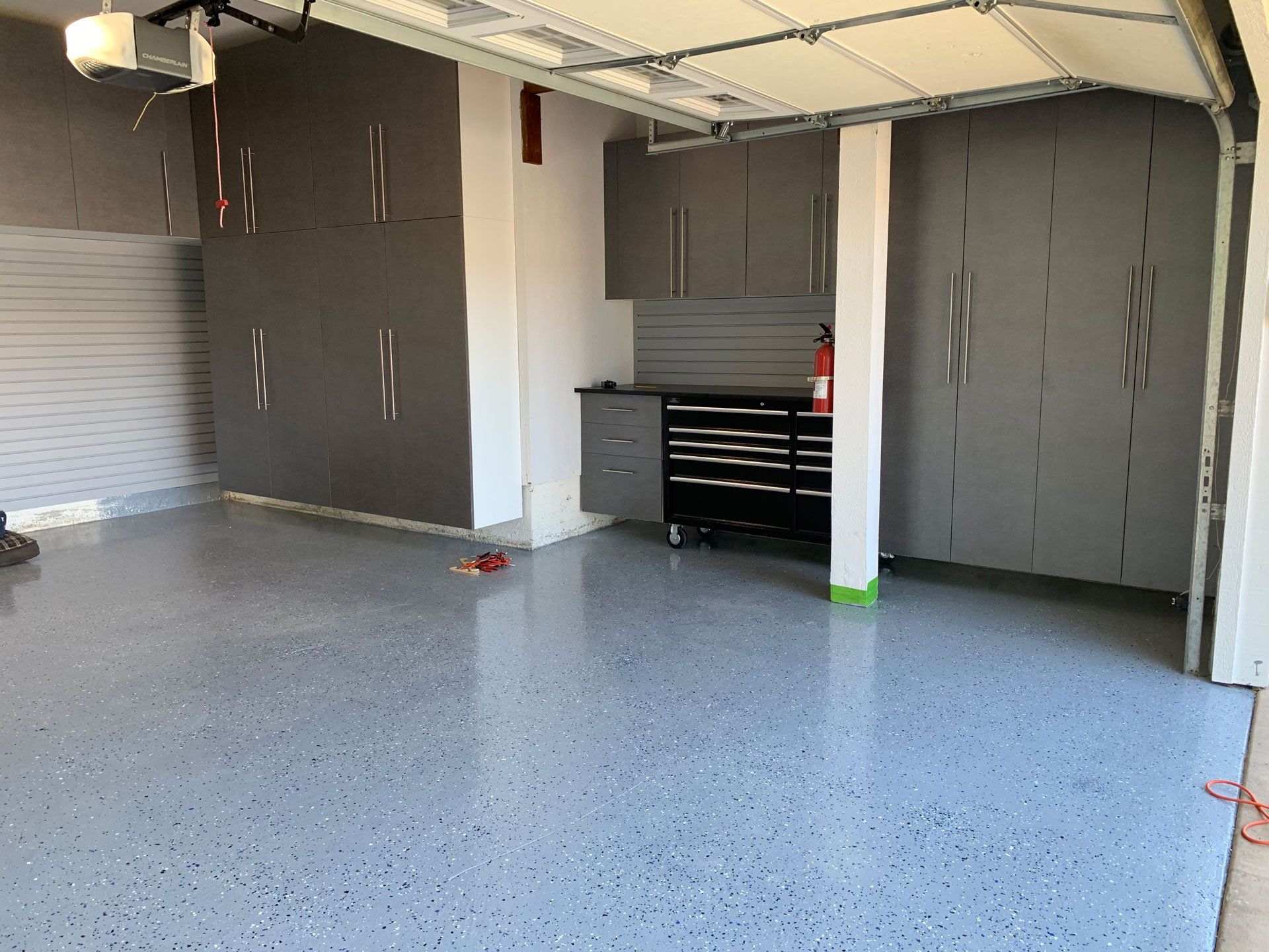 A garage with a garage door open and a fire extinguisher on the floor.