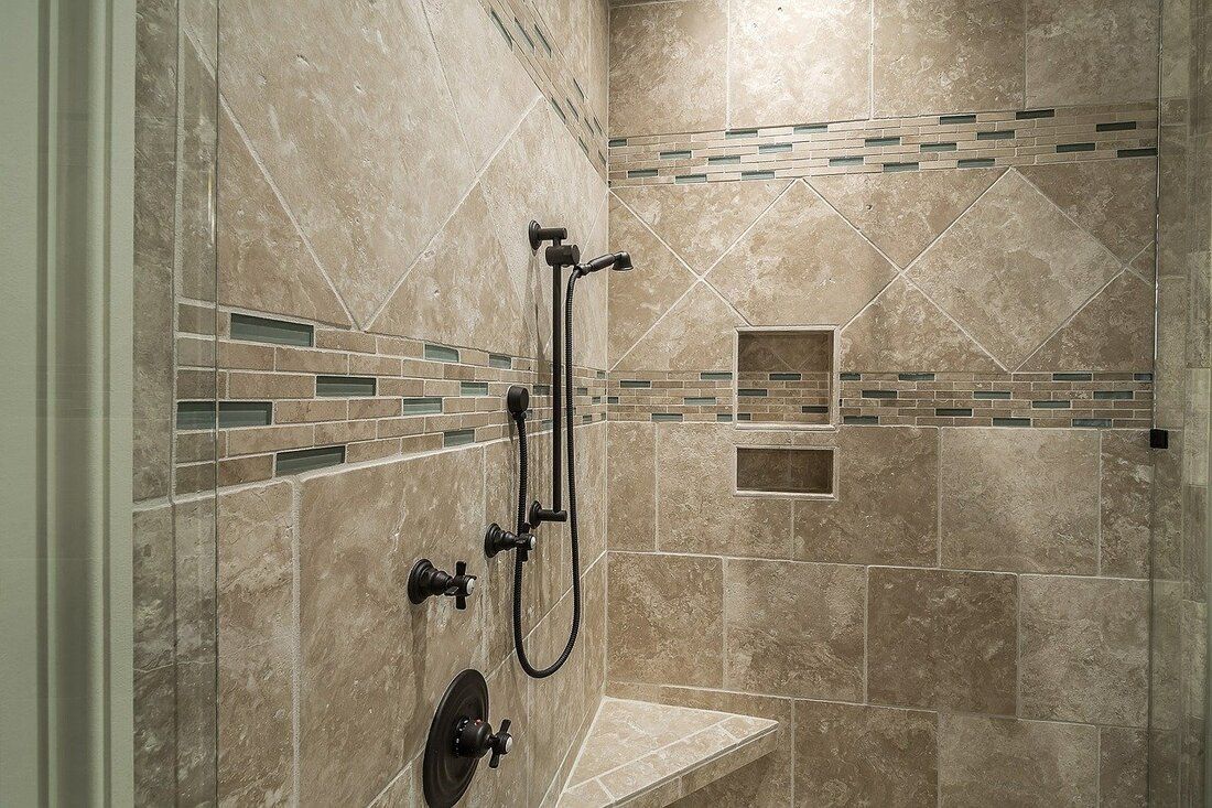 A clawfoot bathtub underneath a window in a bathroom with newly installed marble tile floors and tile walls