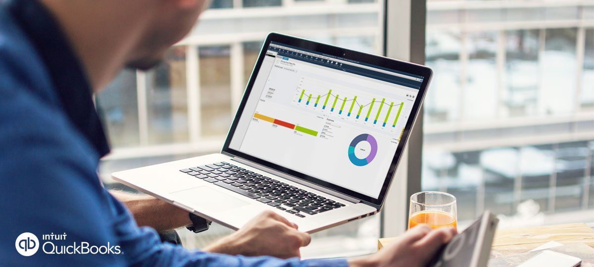 Una persona trabaja en un ordenador portátil que muestra gráficos y tablas de datos en un entorno de oficina con vistas a la ciudad.