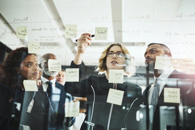 Equipo de negocios colaborando y realizando una lluvia de ideas con notas adhesivas en una pizarra transparente.