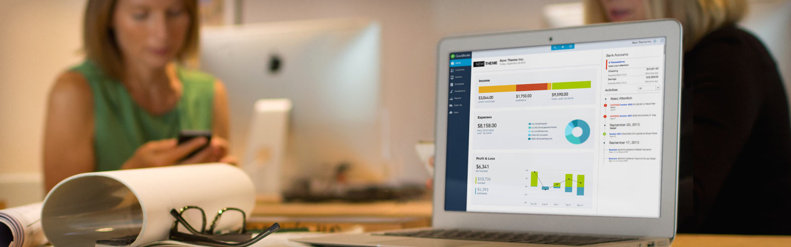 Pantalla de un portátil que muestra un panel de análisis empresarial con gráficos y datos, sobre un escritorio con personas trabajando al fondo.