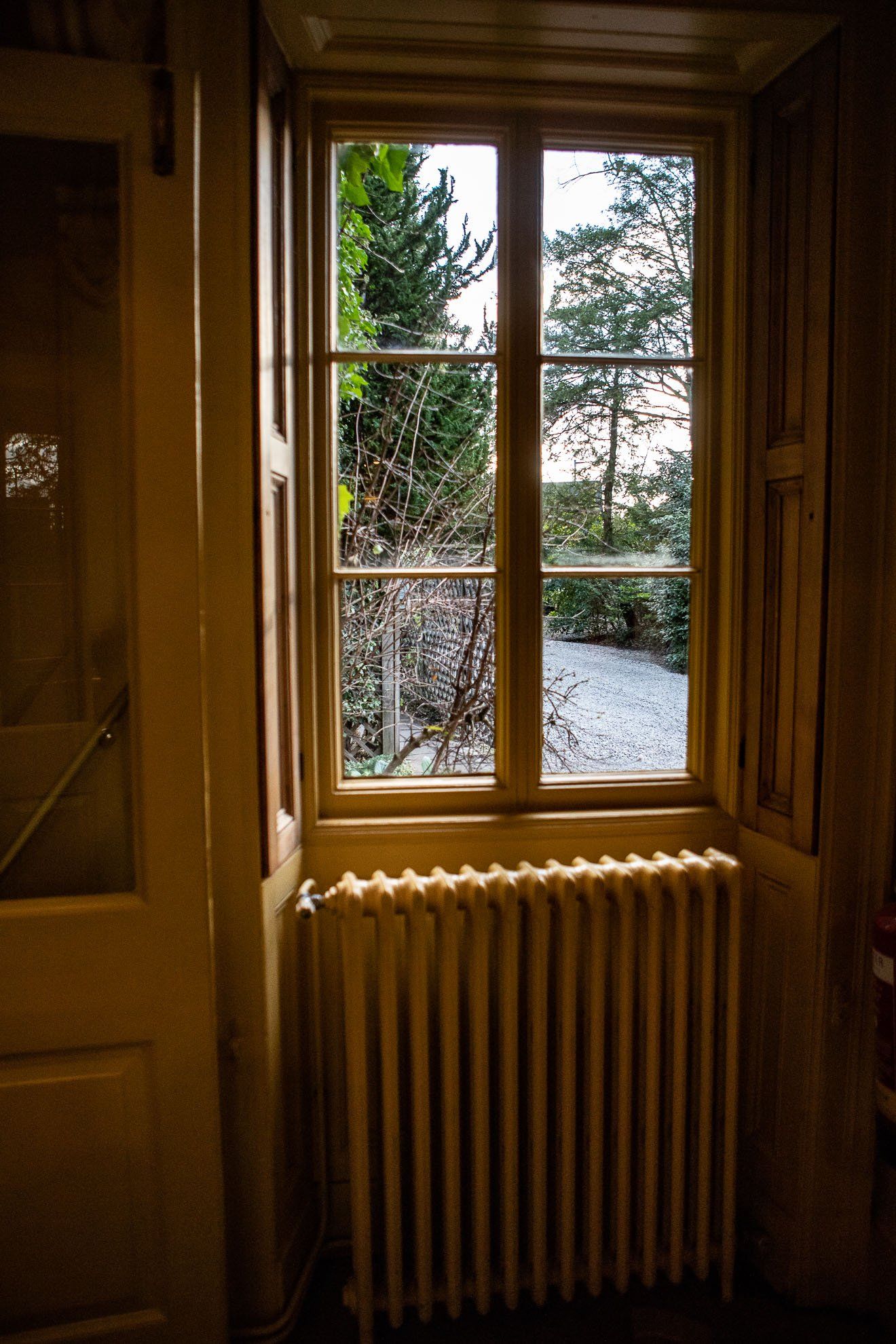 A room with a radiator and a window with a view of a garden.