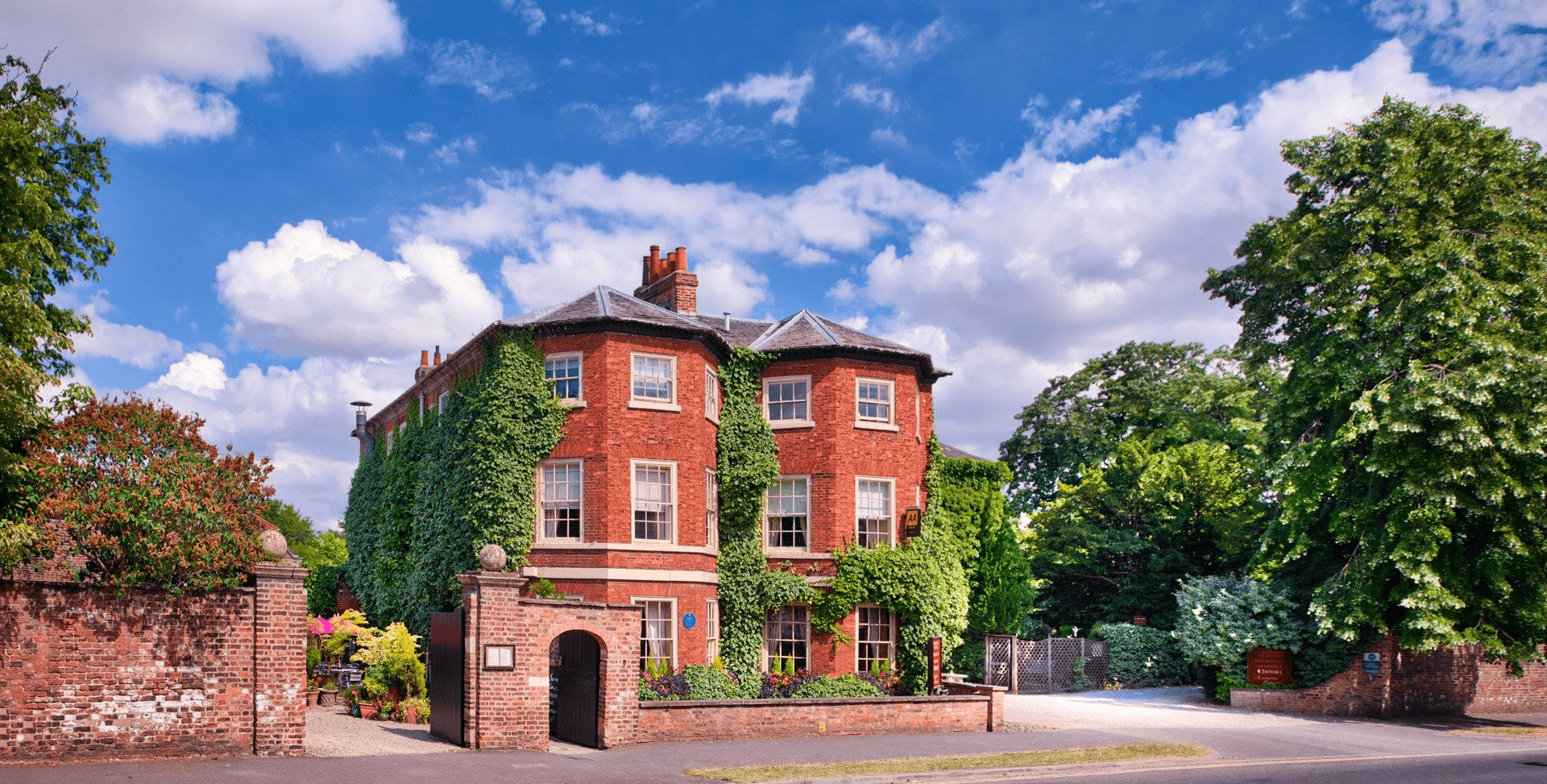 A large red brick house surrounded by trees on a sunny day.
