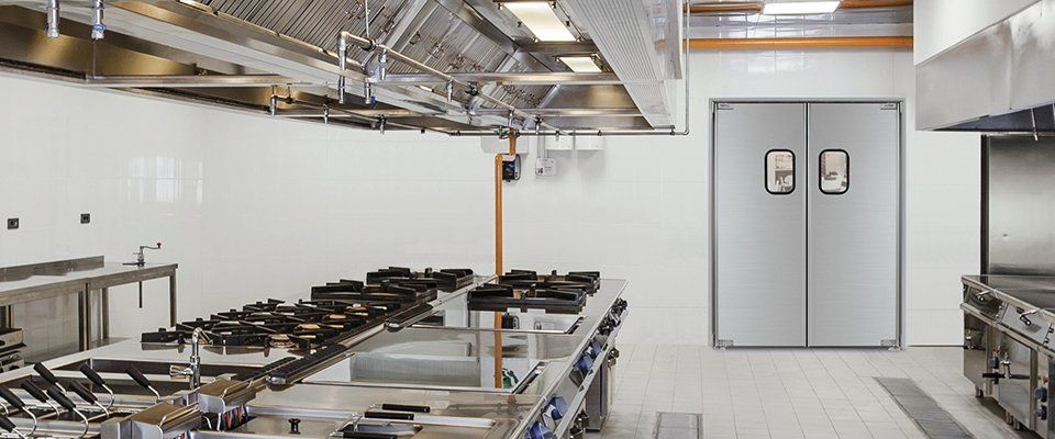 A large commercial kitchen with stainless steel appliances and a double door.