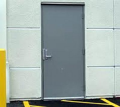 A gray door is sitting on the side of a building next to a yellow barrier.