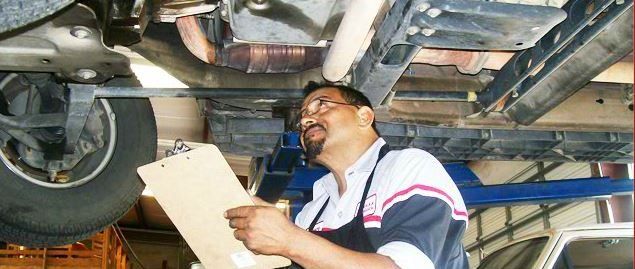 Mechanic inspecting a car undercarriage while holding a clipboard in a repair shop
