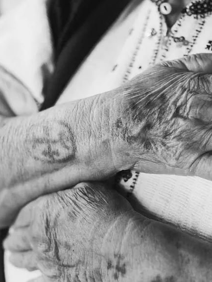 Ein Schwarzweißfoto des Handgelenks einer älteren Frau mit einer Tätowierung darauf.