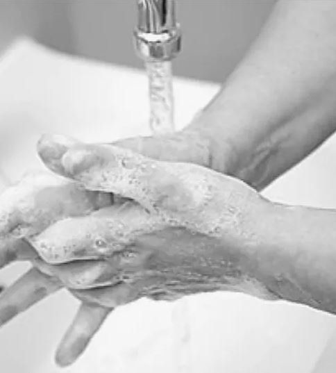 Auf einem Schwarzweißfoto wäscht sich eine Person unter einem Wasserhahn die Hände.